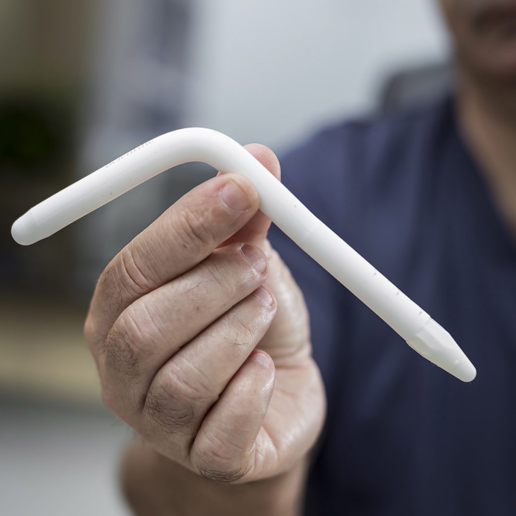 Médico urologista segurando peça de prótese peniana em formato de L.