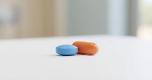 Comprimido azul e cápsula laranja sobre superfície branca representando os medicamentos no tratamento da disfunção erétil