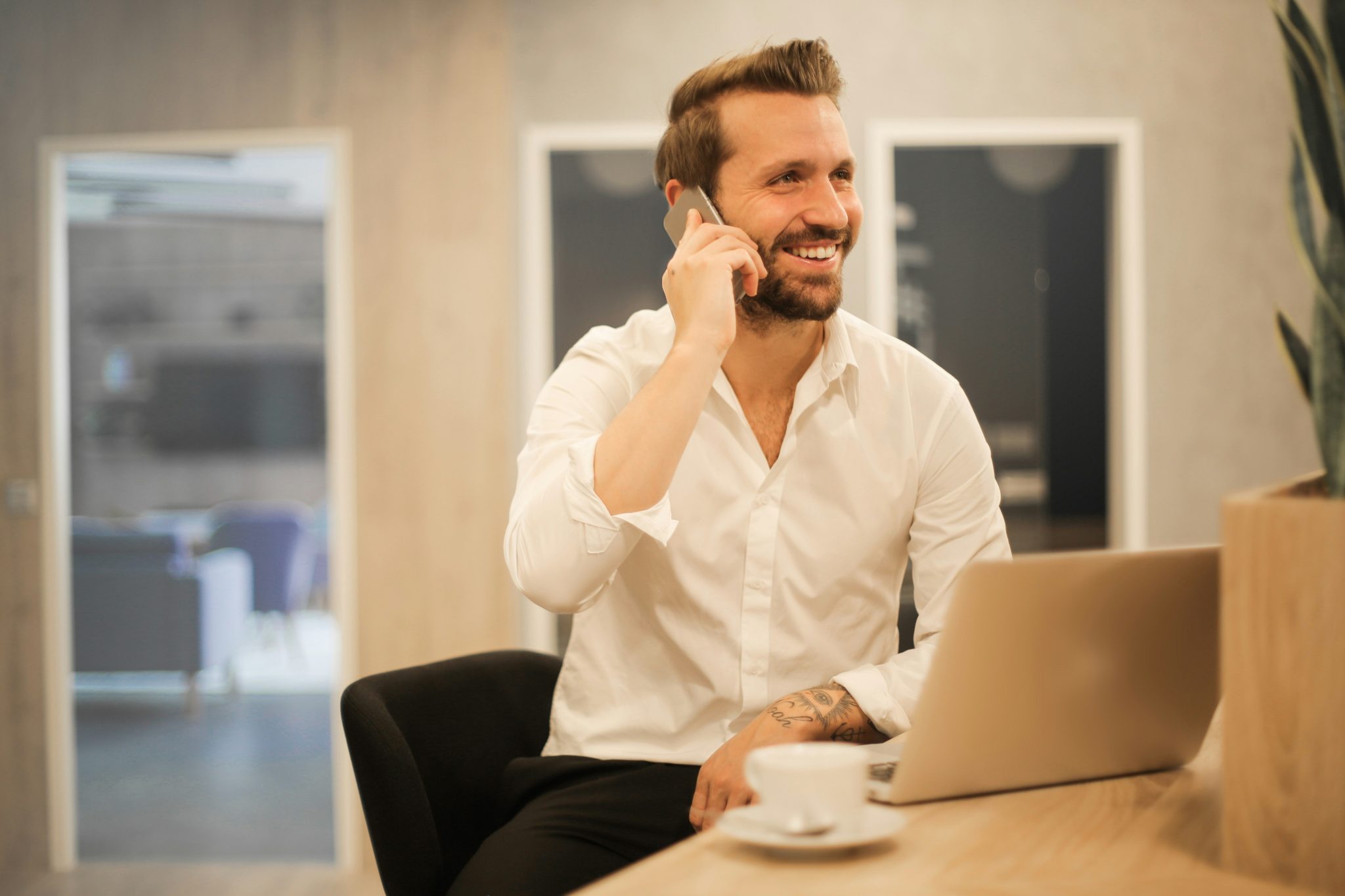 Homem adulto sentado confortavelmente numa cadeira, a olhar para o smartphone que segura com as duas mãos, com roupas casuais e expressão concentrada. O ambiente ao redor é simples e iluminado, transmitindo um momento de uso normal de um dispositivo móvel num espaço interior.