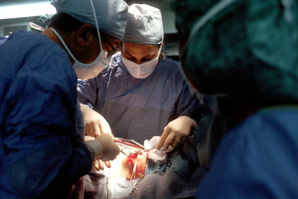 médicos a operar numa sala cirúrgica, com equipamento médico e luzes cirúrgicas, ilustrando uma intervenção especializada em urologia reconstrutiva.