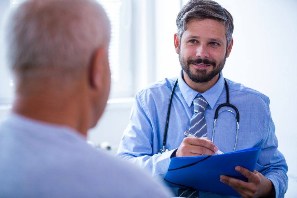 Homem em consulta médica com urologista a analisar informações sobre cirurgia de implante peniano e custos associados.