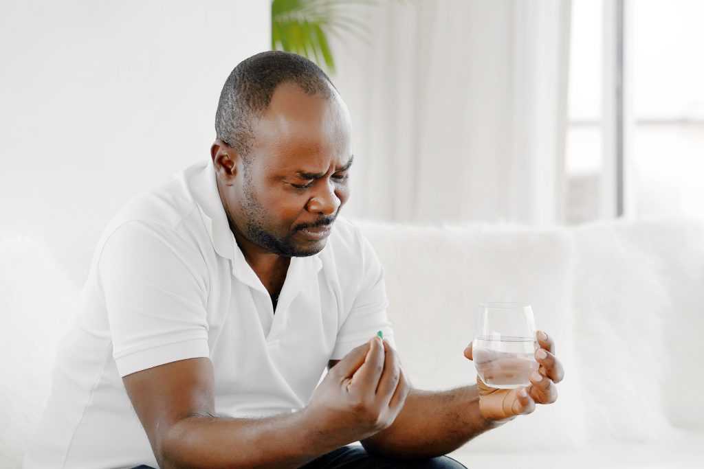 Hombre sentado en casa tomando medicamentos como Sildenafilo y Tadalafilo