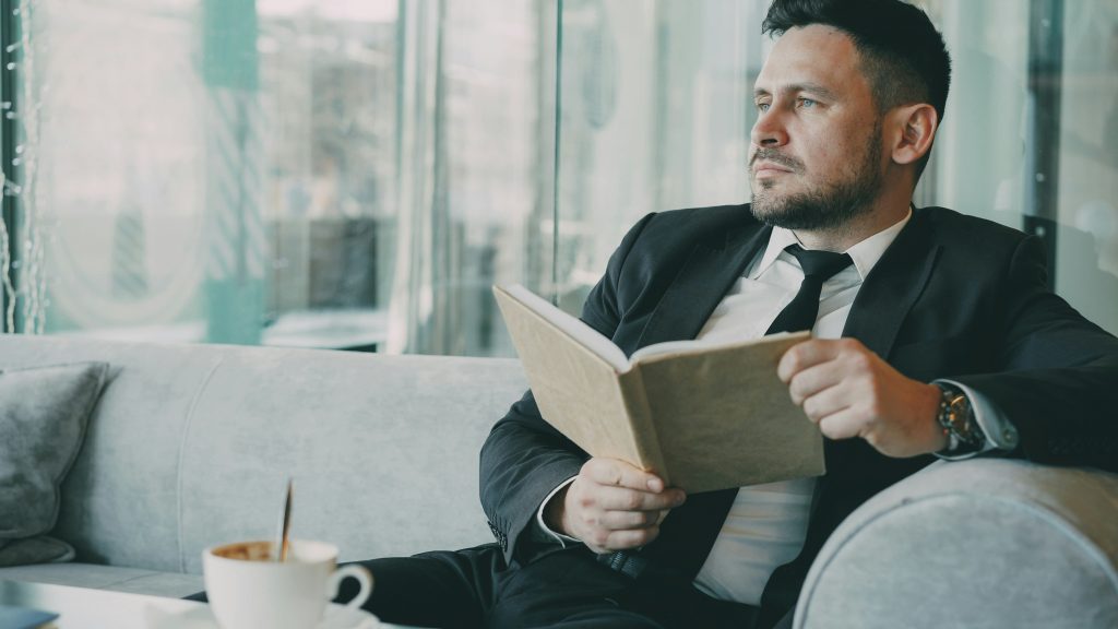 Homem adulto bem-vestido a ler com café, representando ponderação sobre saúde sexual e necessidade de implante peniano