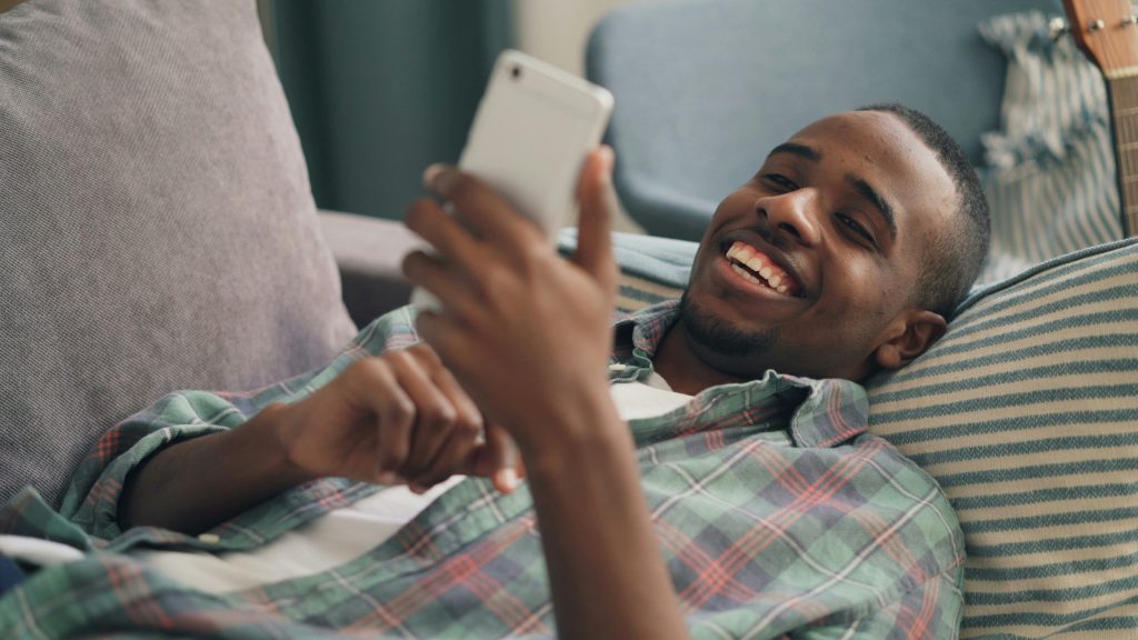 Homem deitado num sofá a olhar para um smartphone, relaxado em casa depois de conhecer a Técnica Egydio