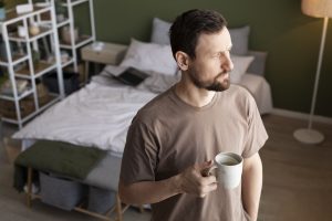 Homem pensativo no quarto com uma caneca na mão, representando o impacto emocional da curvatura peniana congénita na qualidade de vida.