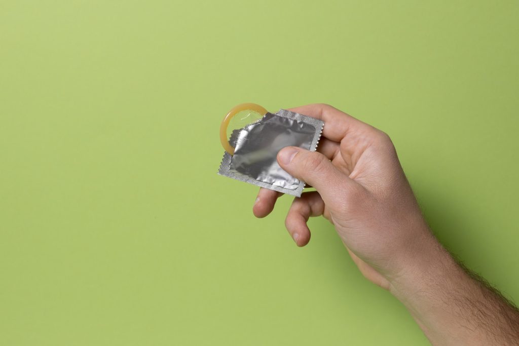 Mano masculina con preservativos envasados sobre fondo verde, que representa la importancia del uso de preservativo en el sexo anal