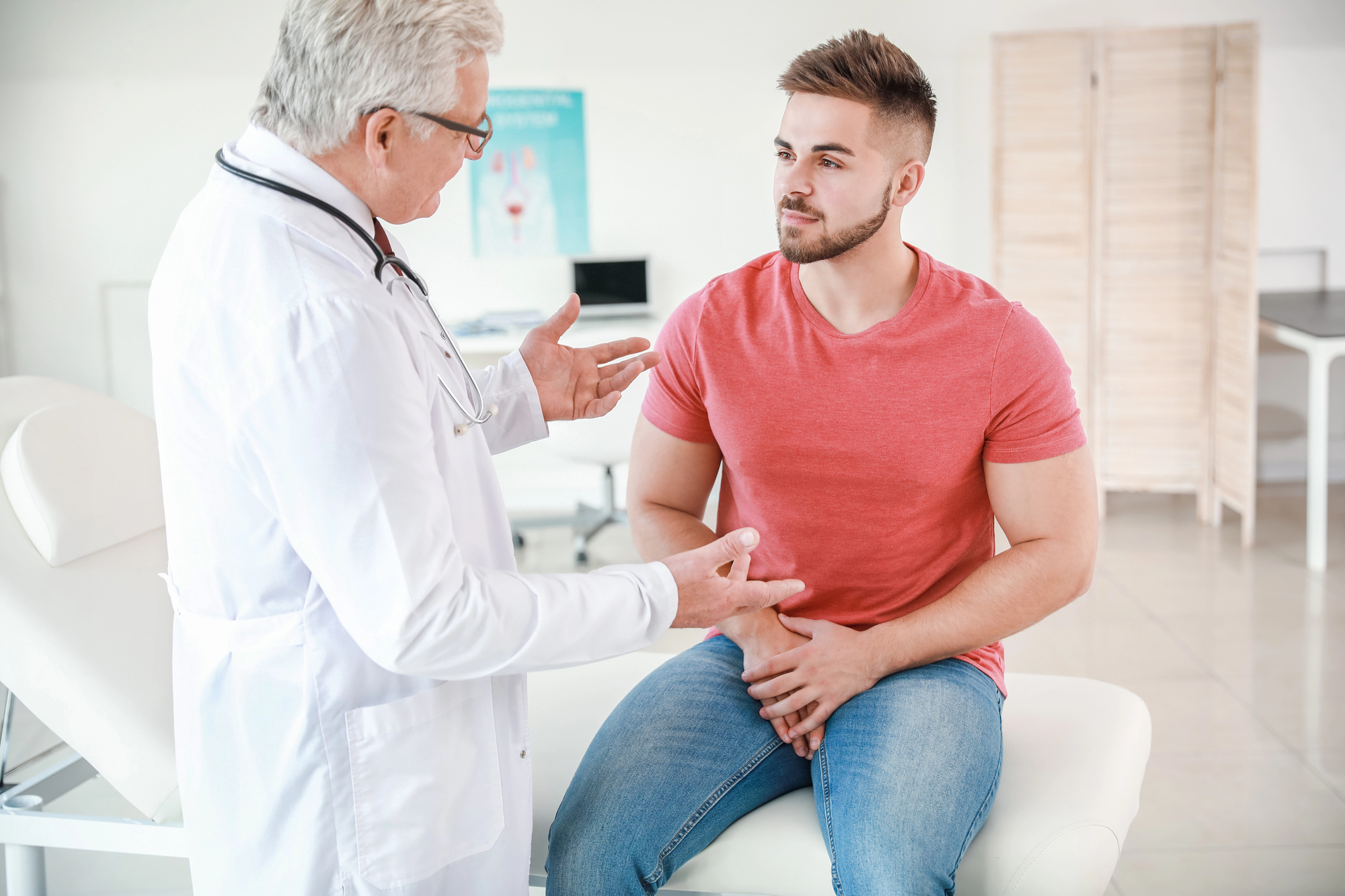 Médico urologista apresenta resultados de exames de prótese peniana insuflável durante uma consulta, explicando a sua durabilidade, funcionamento e longevidade a um doente homem.