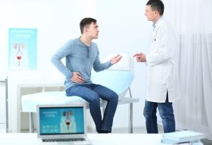 Médico urologista explica, através de um modelo anatómico, como a Doença de Peyronie pode provocar encurtamento peniano e deformidades associadas durante uma consulta especializada.