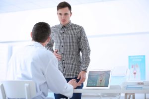 Médico urologista esclarece um doente sobre sensibilidade e prazer sexual após a cirurgia de prótese peniana, utilizando um modelo anatómico durante uma consulta.